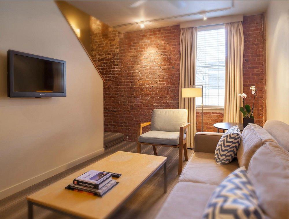 Cozy living room with brick walls, sofa, armchair, TV, and window light.