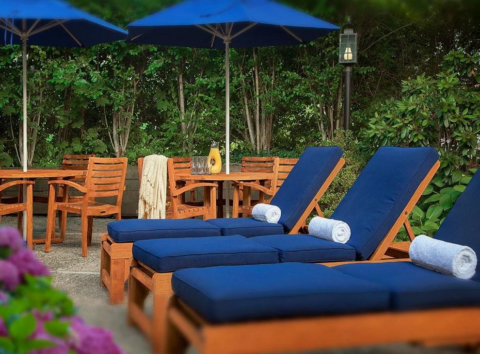 Poolside loungers with blue cushions under umbrellas, surrounded by greenery.