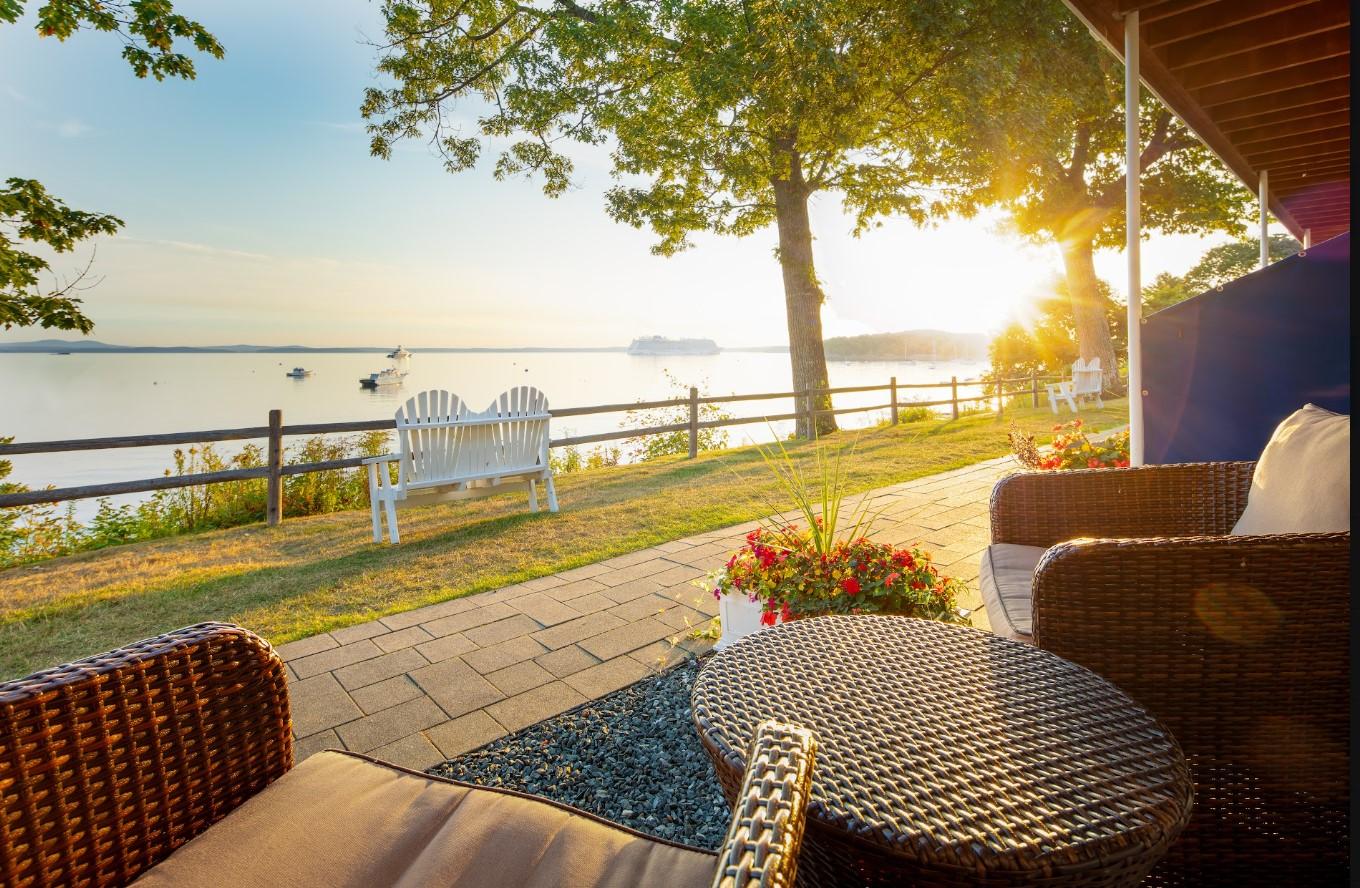 Sunlit patio with wicker chairs, overlooking a serene lake at sunset.