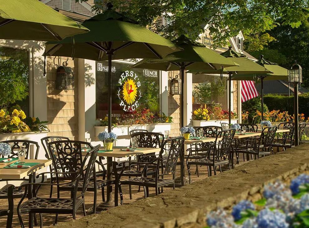 Outdoor patio with tables, green umbrellas, and flowers under sunny skies.