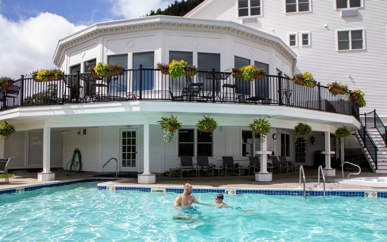 Outdoor pool with two people swimming, surrounded by a white building with balconies.