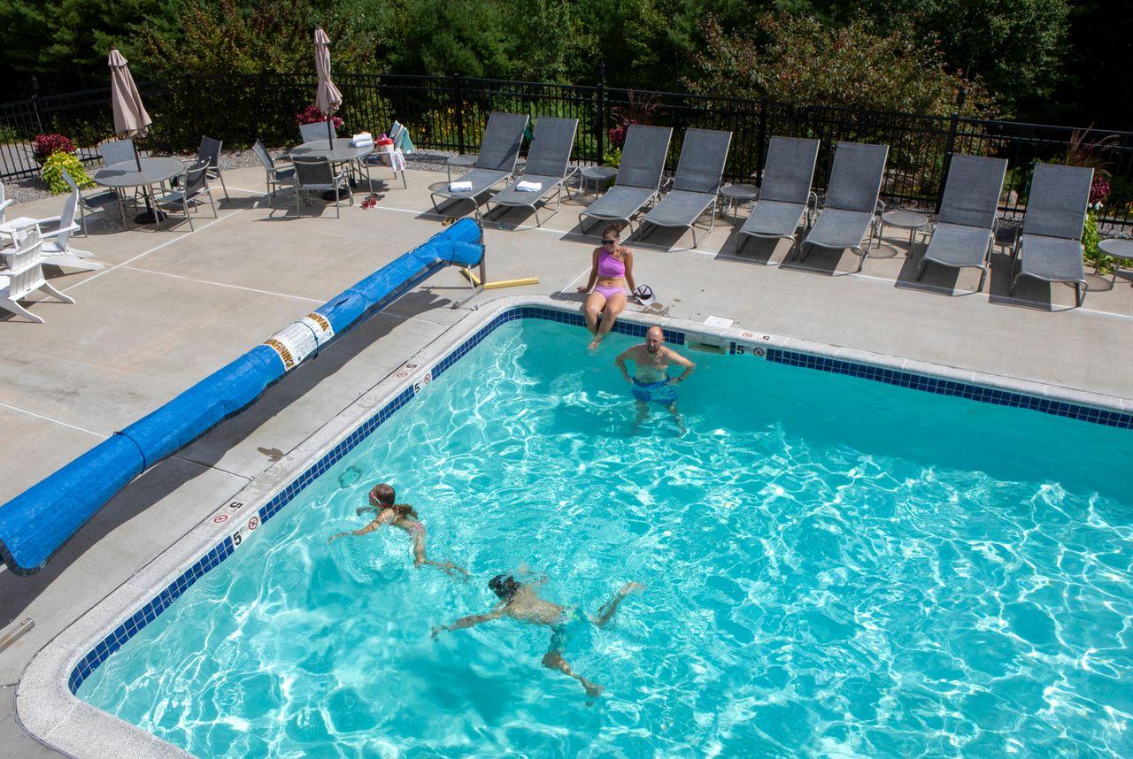 Outdoor pool with people swimming, surrounded by lounge chairs.