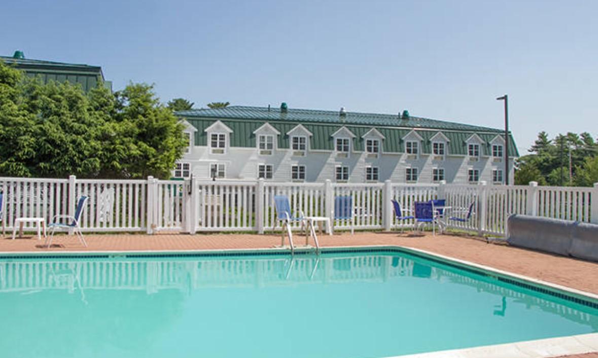 Outdoor pool with white fence, chairs, and a building in the background.