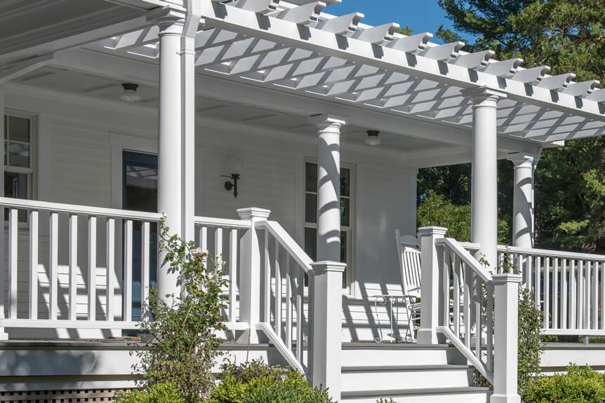 White porch with railing and pergola, surrounded by greenery.