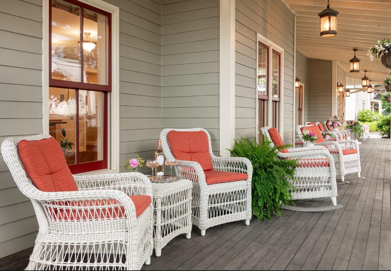 Wicker chairs with red cushions on a porch with hanging lanterns.