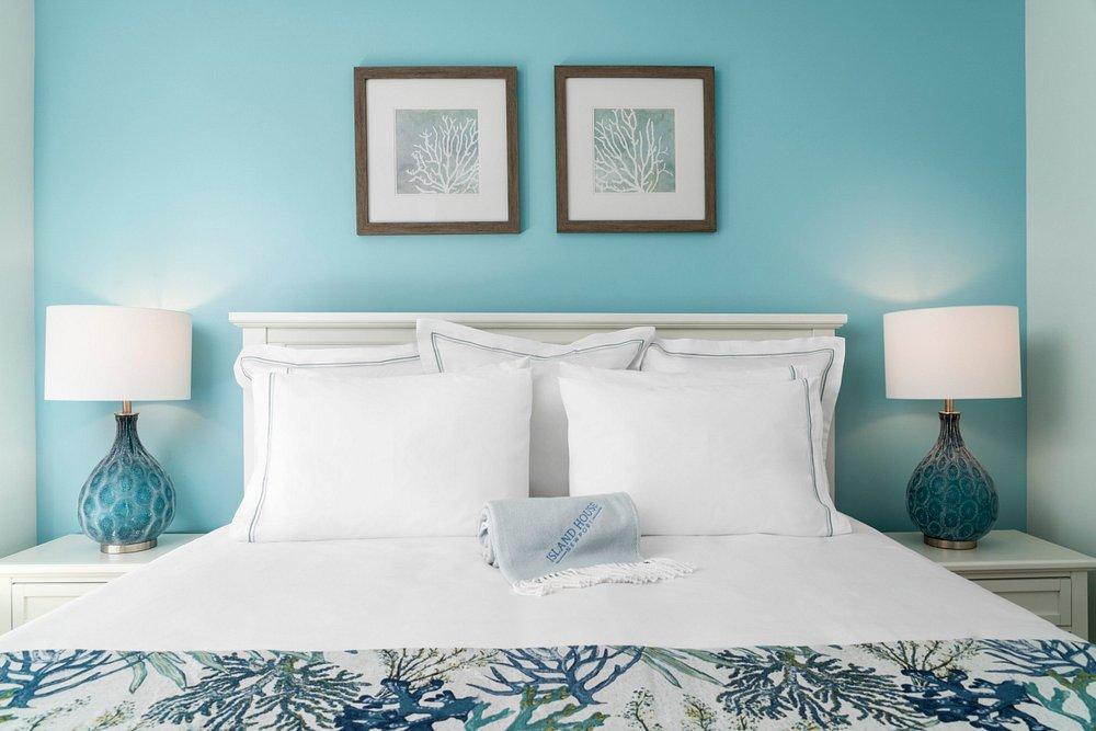 Bedroom with teal walls, white bed, two lamps, and framed art above the headboard.