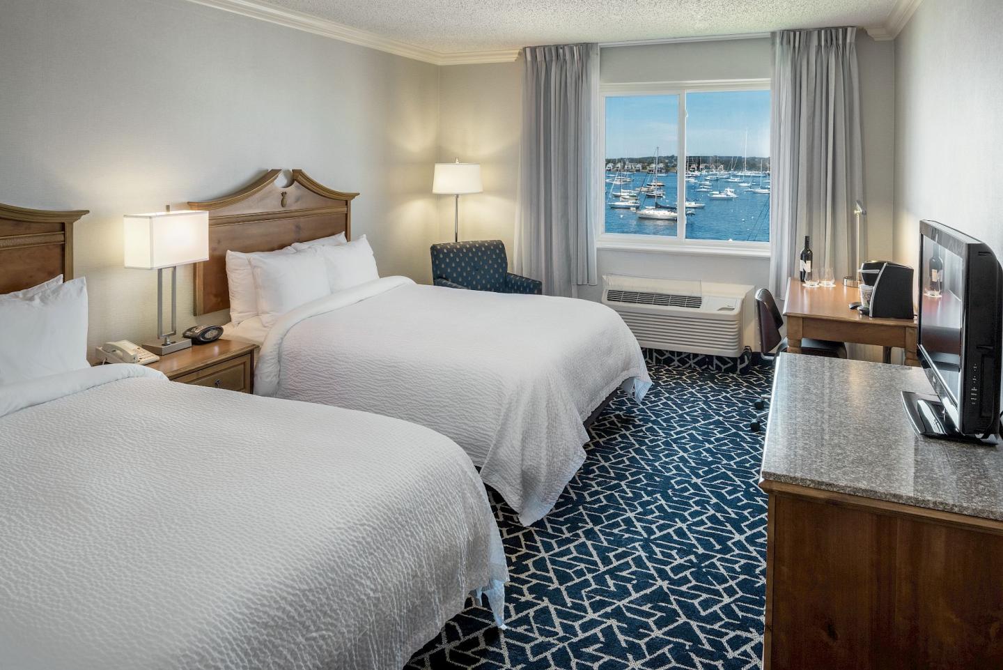 Two-bed hotel room with ocean view, TV, and desk.