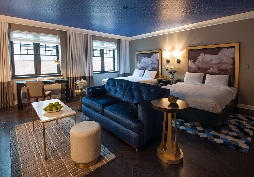 Modern hotel room with two beds, blue sofa, and a dining table.