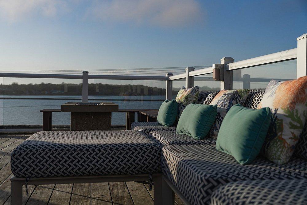 Deck with cushioned seating and pillows overlooking a calm water view.