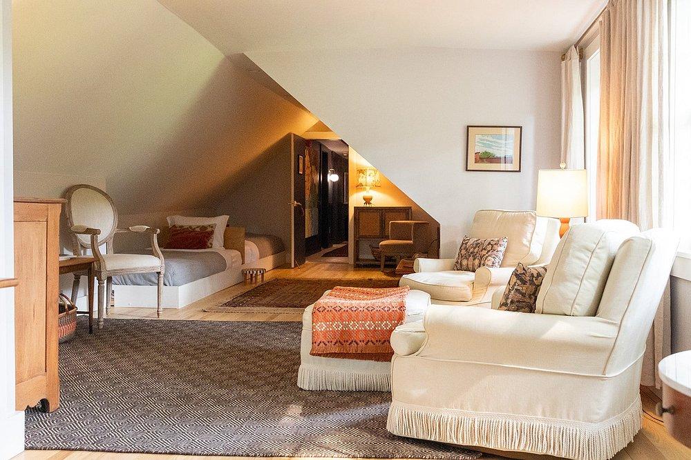 Cozy attic room with armchairs, a bed, and warm lighting.