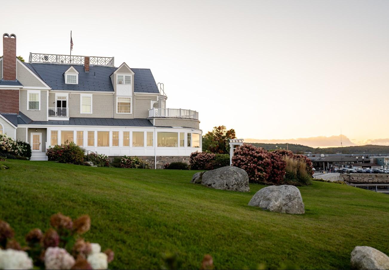 Large house on green lawn near the water, under a clear sky at sunset.