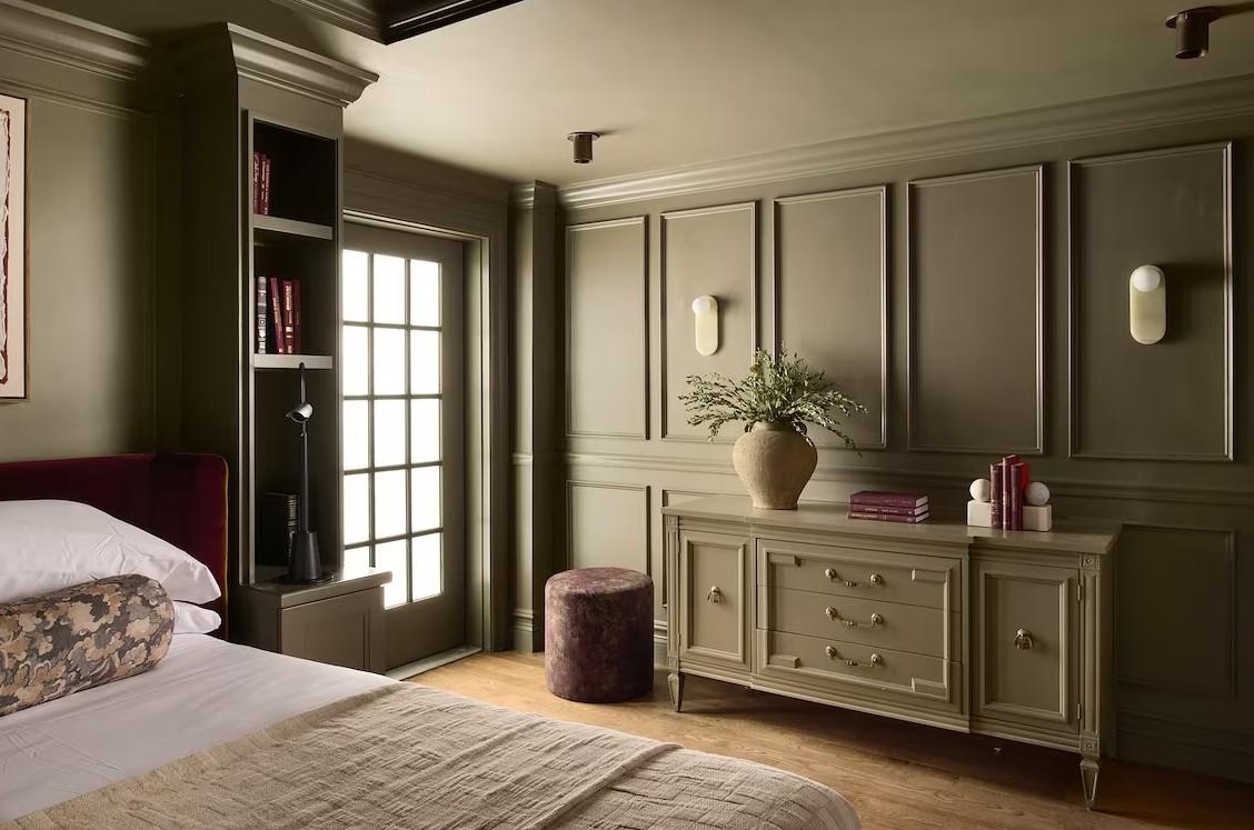 Elegant bedroom with olive walls, a bed, dresser, and soft lighting.
