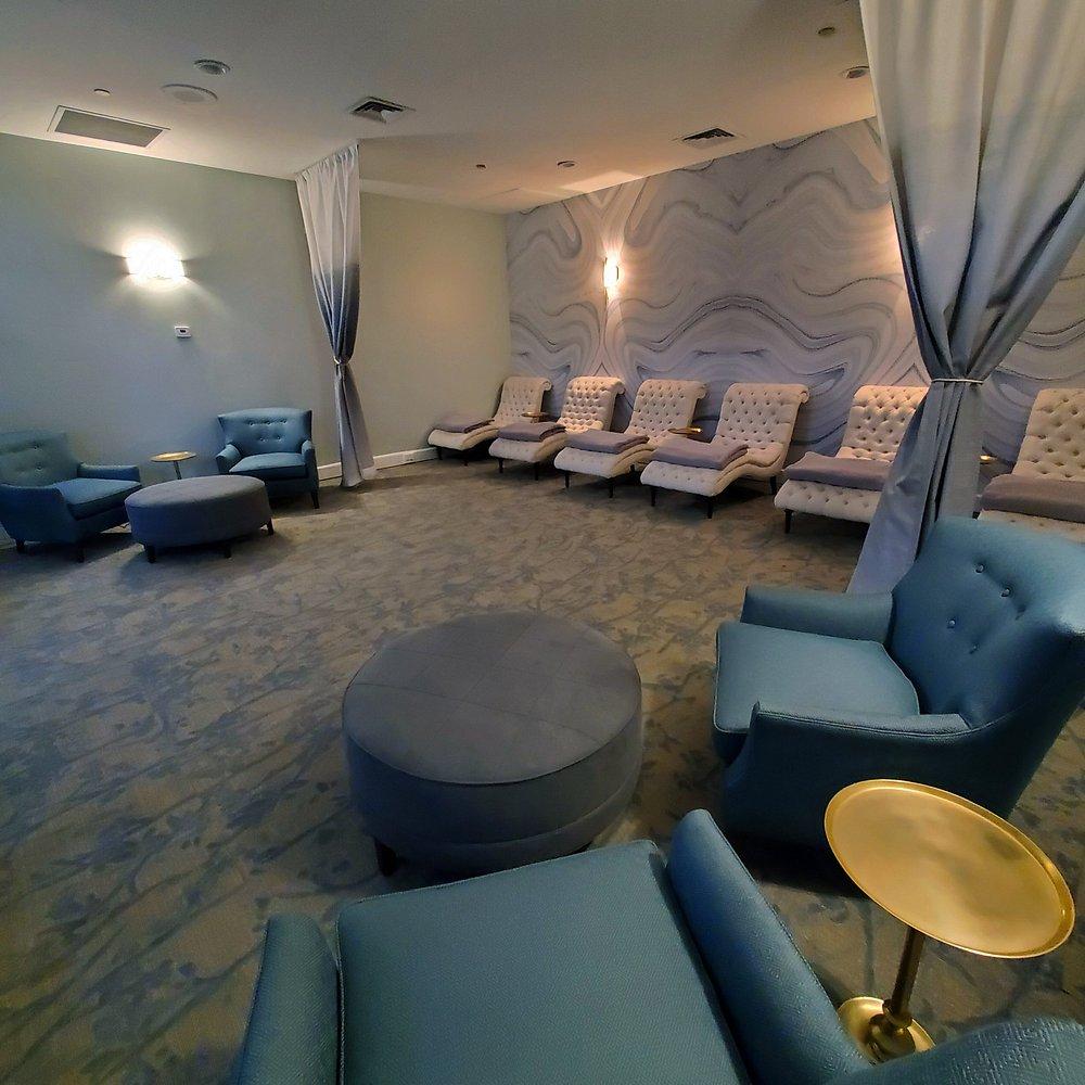 Spa lounge with blue chairs, ottomans, and soft lighting.