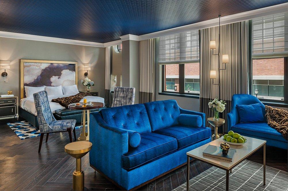 Luxurious hotel room with blue sofas, elegant decor, and a cozy bed in warm lighting.