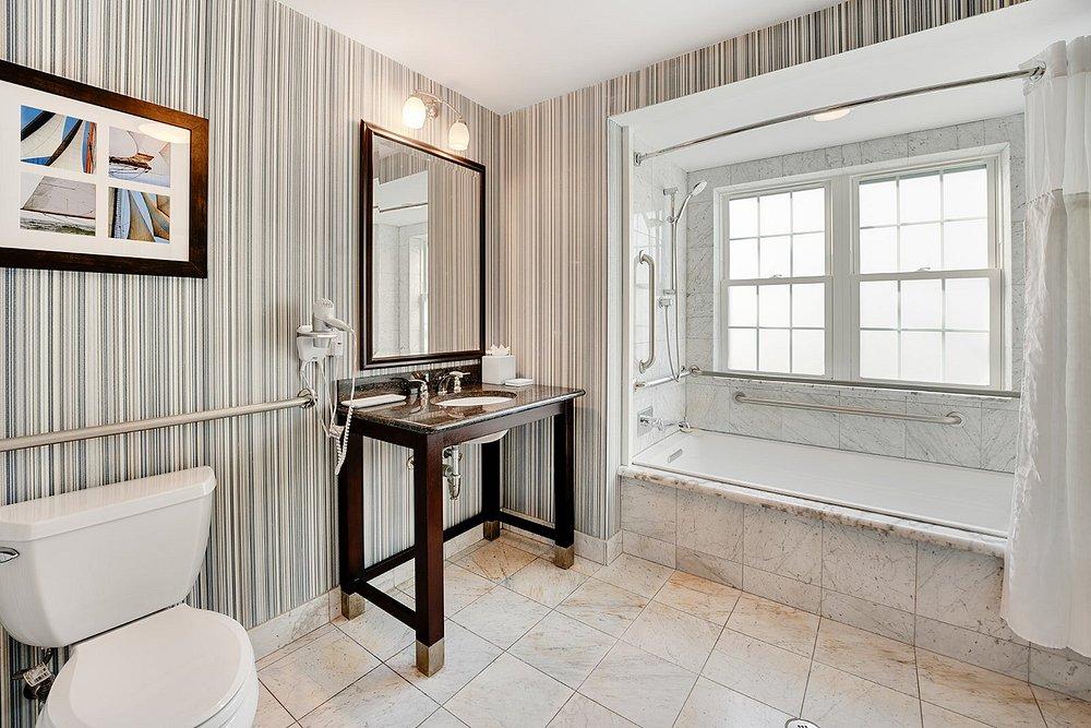 Elegant bathroom with striped walls, large mirror, and a window beside a bathtub.