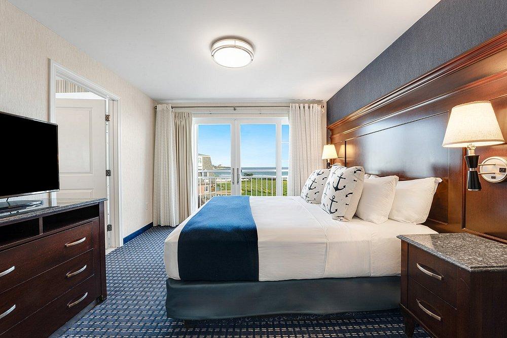 Cozy hotel room with a king bed, TV, and ocean view balcony.