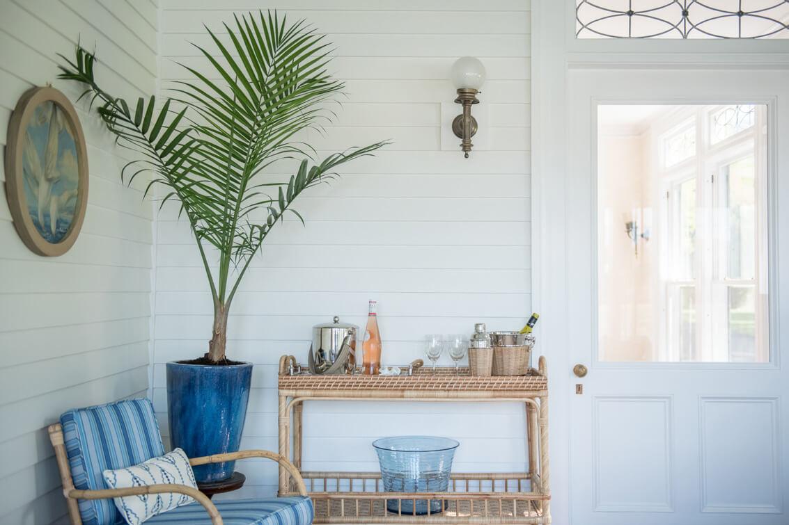 Cozy porch with a wicker chair, a potted palm, and a side table with drinks.