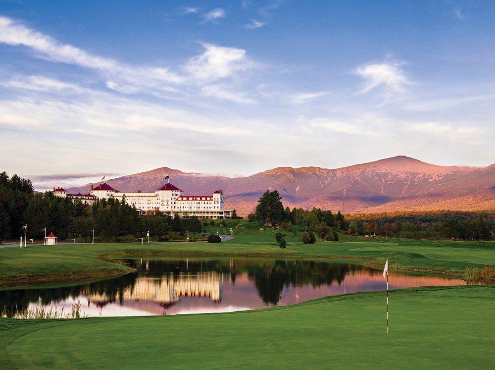 Elegant hotel by a lake, with mountains in the sunset in the background.