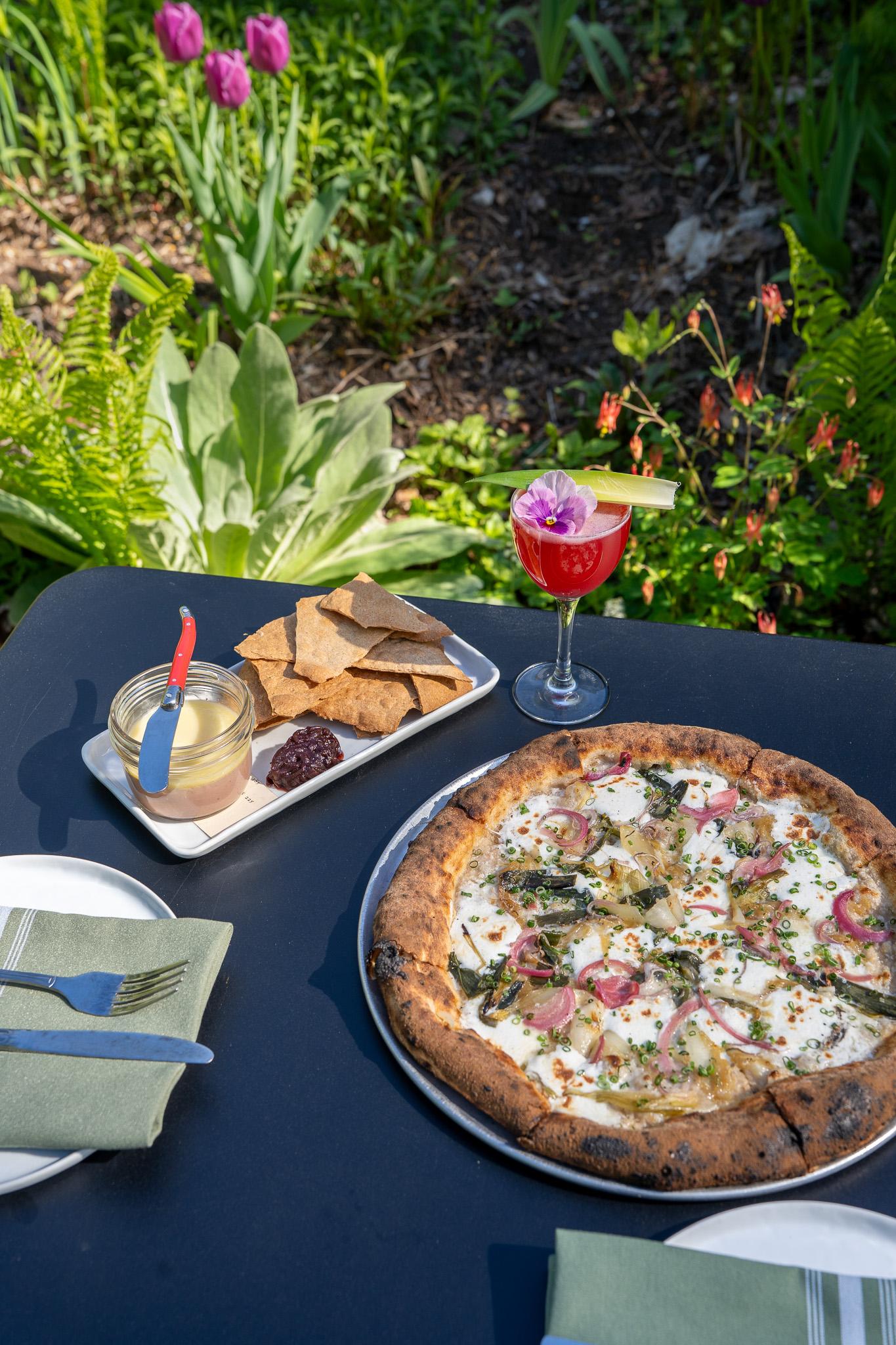Pizza and a cocktail on a table outdoors in a garden setting.