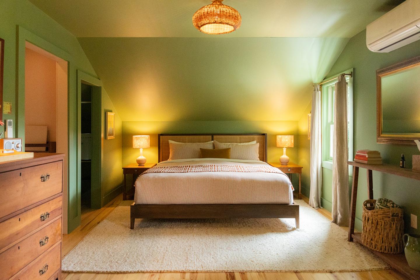 Cozy bedroom with green walls, a bed, soft lighting, and wooden furniture.