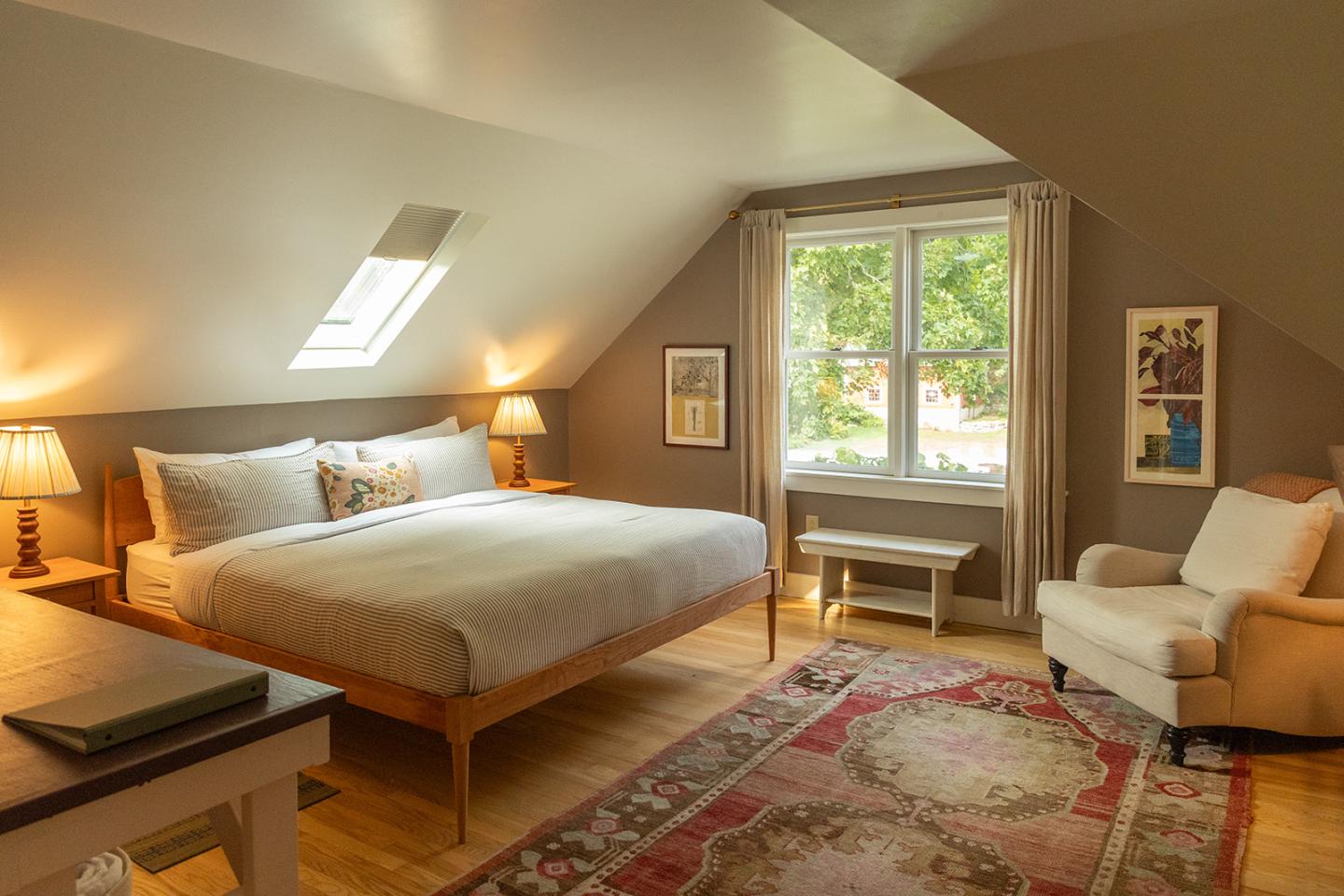 Cozy attic bedroom with large bed, armchair, and warm lighting.