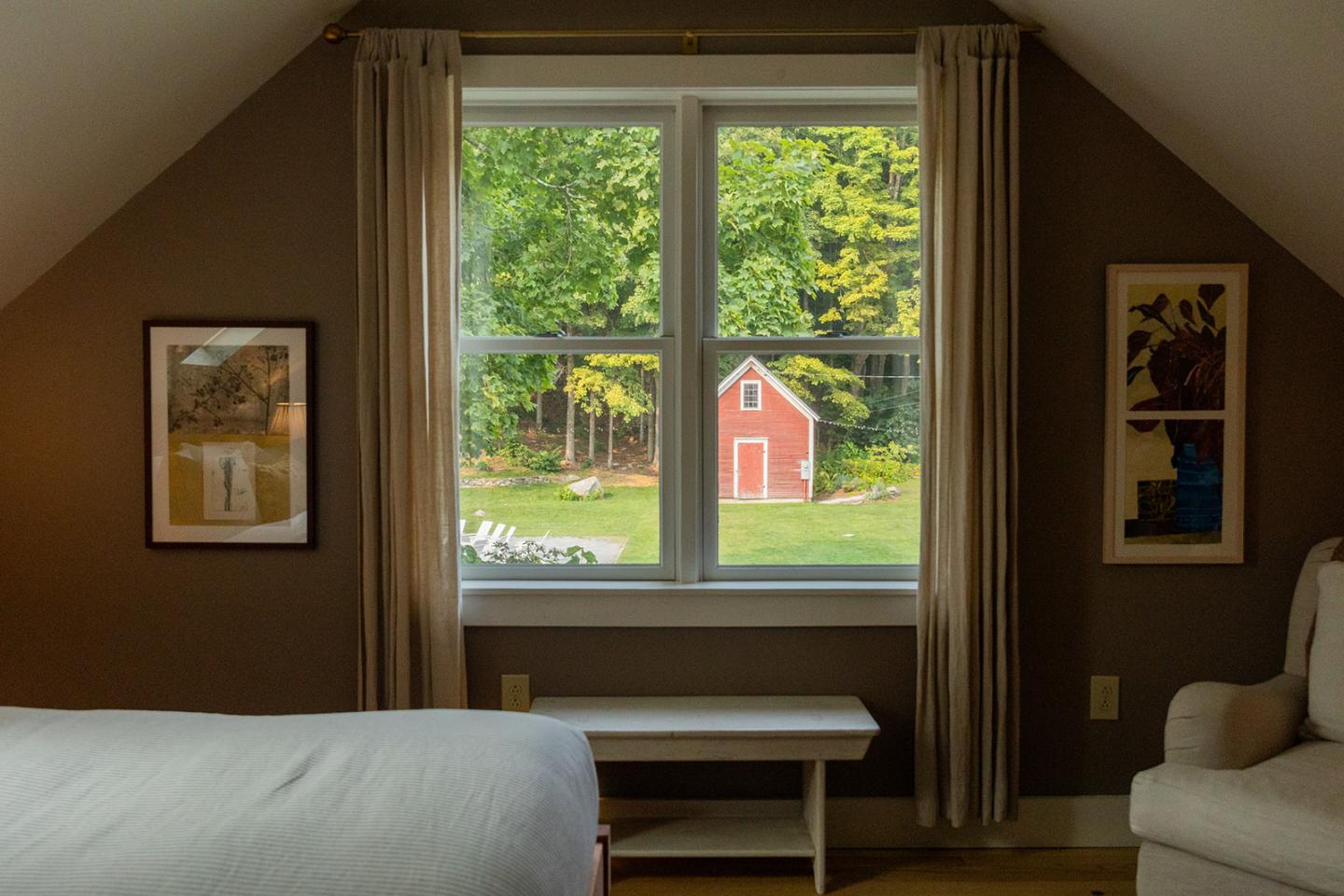 Cozy bedroom with a window view of a red barn in a green yard.