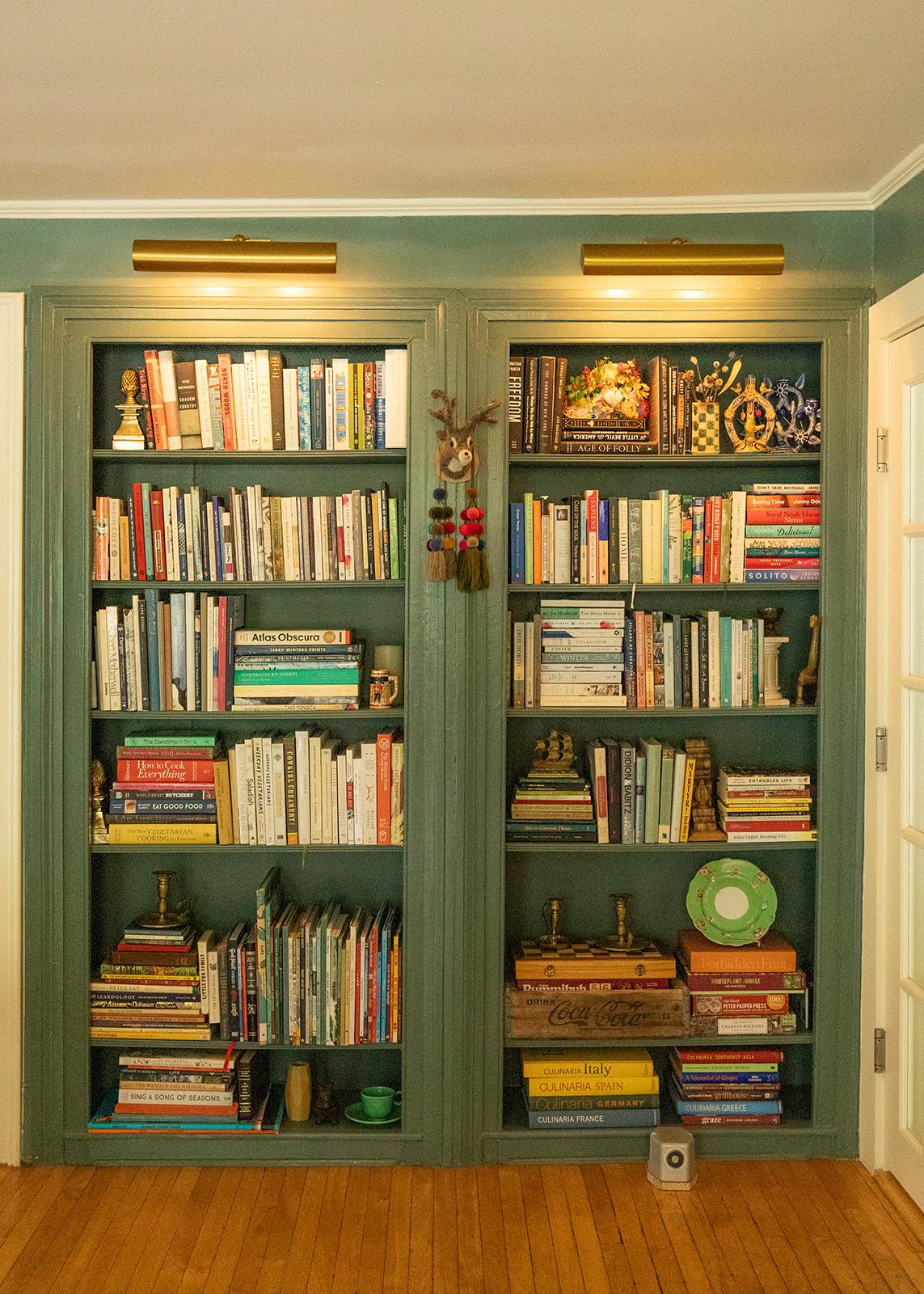 Green bookcase filled with books and decorative items, wooden floor, warm lighting.