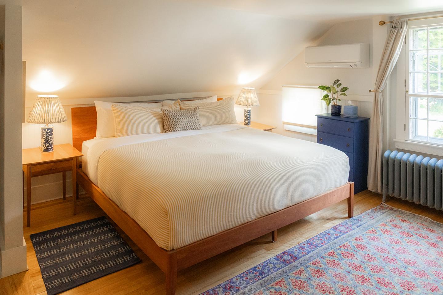 Cozy bedroom with a large bed, soft lighting, and a blue dresser by the window.