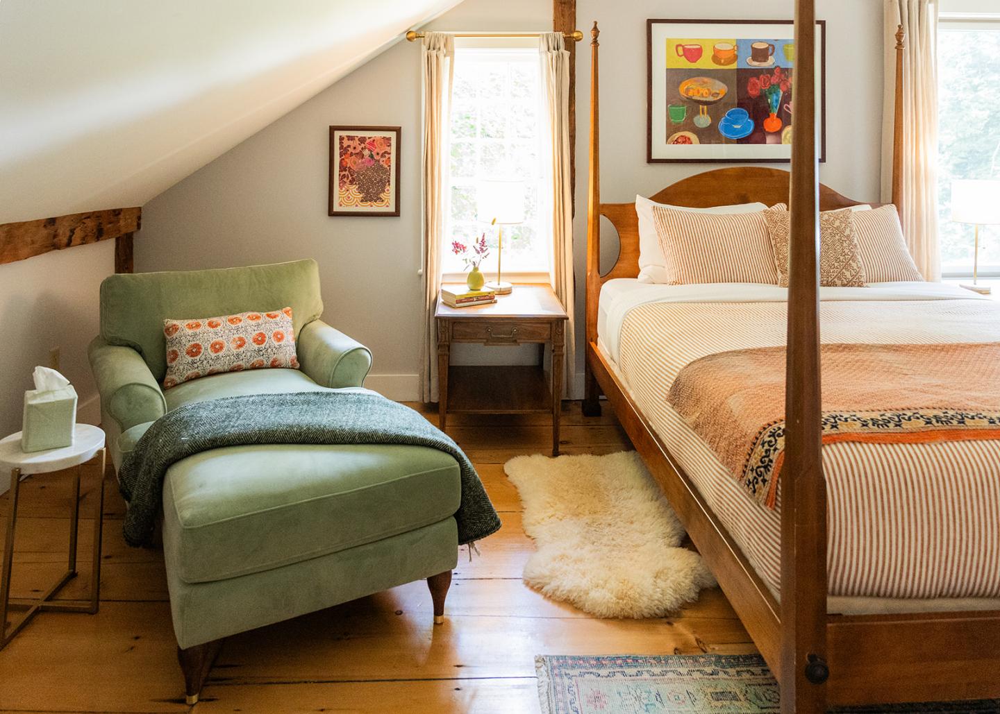 Cozy bedroom with a green chaise, wooden bed, and colorful wall art.
