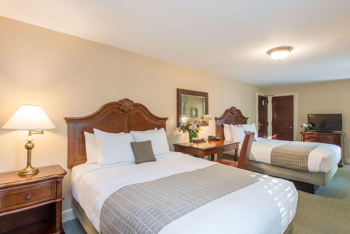 Two double beds in a hotel room with warm lighting and a wooden dresser.