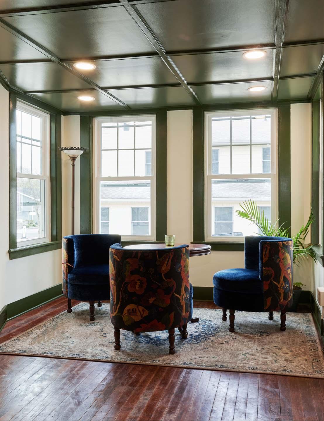 Cozy seating area with two blue chairs, a small table, and green plant by large windows.