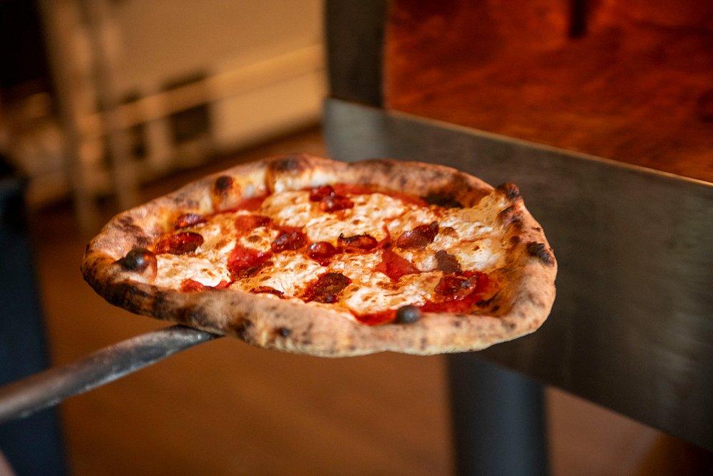 Pizza on a paddle being placed in a wood-fired oven.