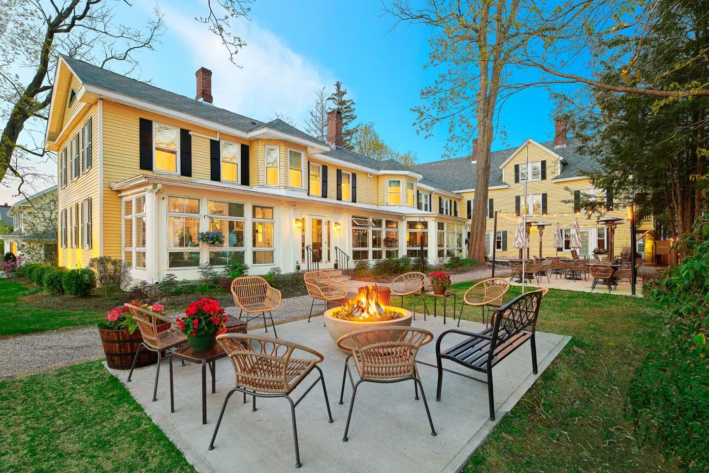 Yellow house with a patio, chairs around a fire pit, and string lights at twilight.