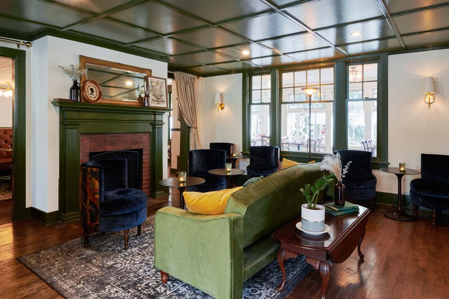 Cozy living room with green sofa, dark chairs, and fireplace.