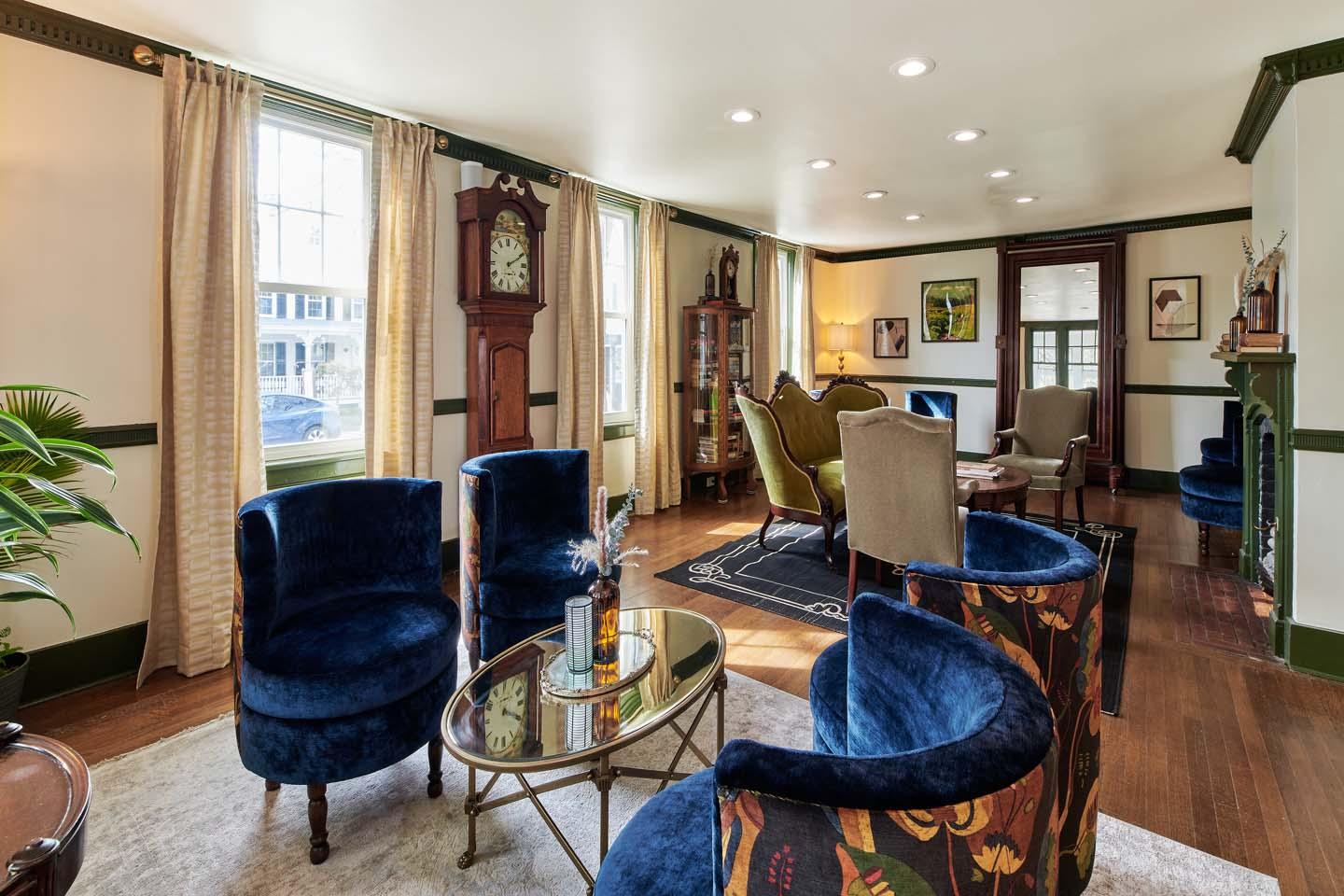 Cozy living room with blue velvet chairs, wooden floors, and a grandfather clock.