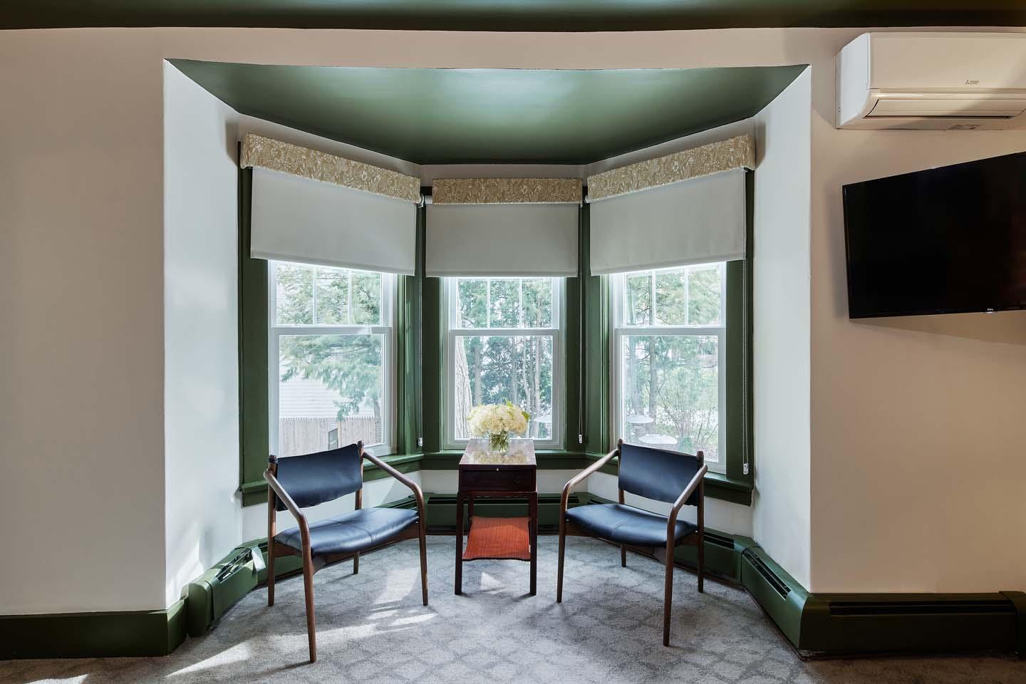 Two chairs and a table in a bay window with greenery outside.