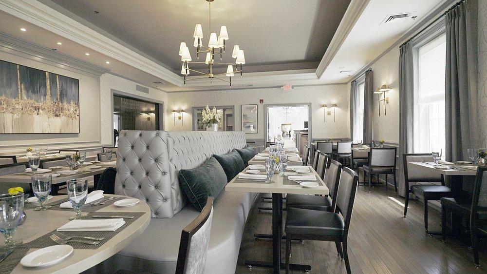 Elegant restaurant interior with chandeliers, light grey seating, and white table settings.