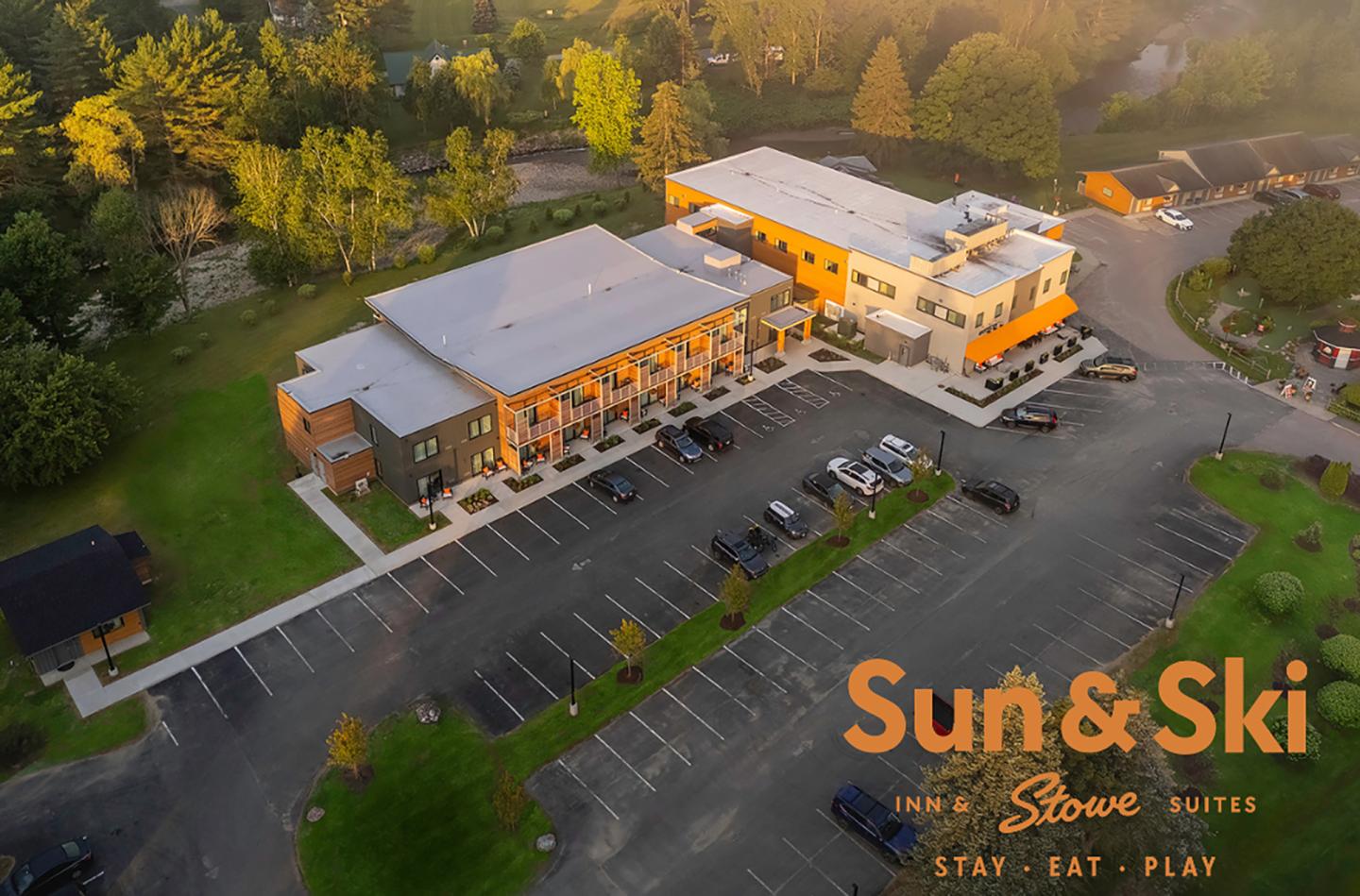 Aerial view of a hotel with parking lot surrounded by trees.