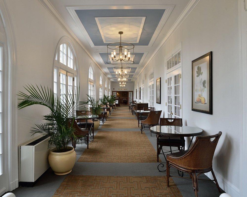 Bright hallway with chandeliers, plants, and wicker chairs along the walls.