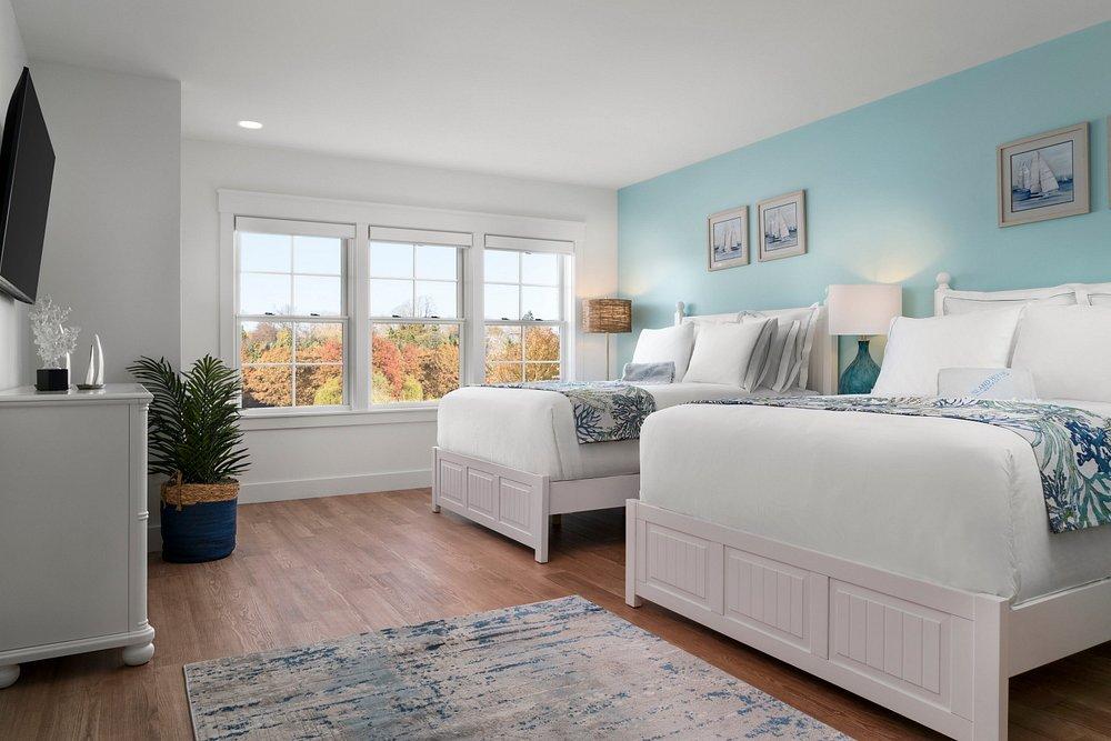 Modern bedroom with two white beds, blue accent wall, and large window.