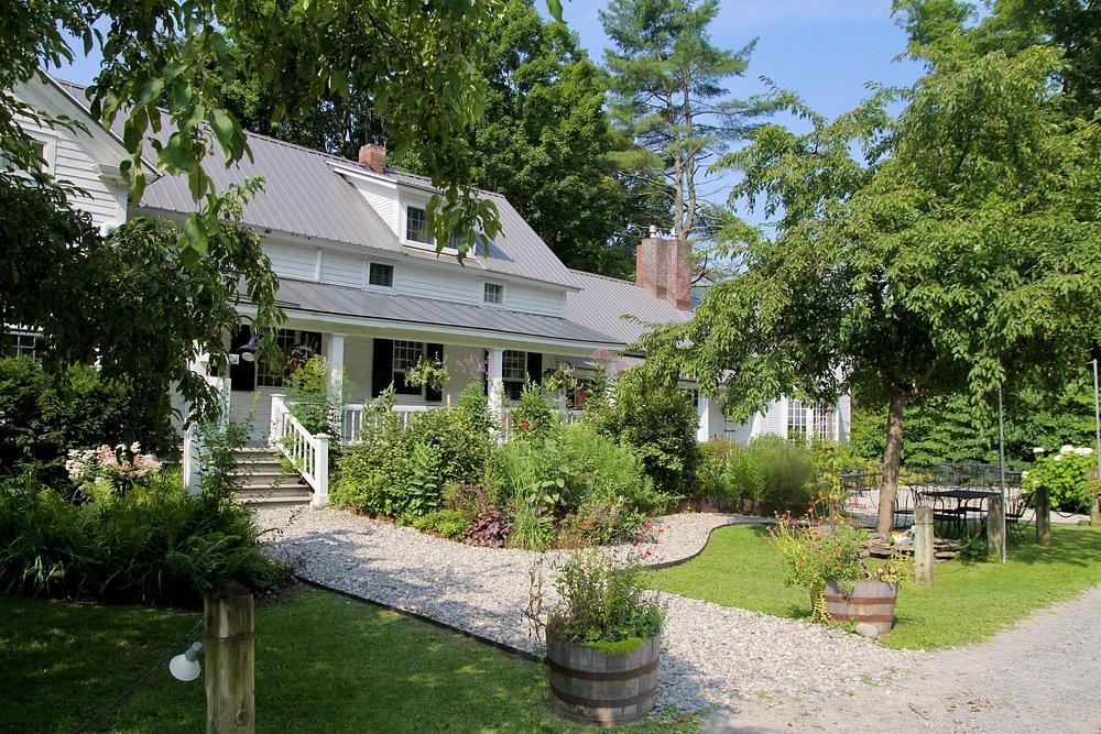 White house with a porch, surrounded by lush greenery and stone path.