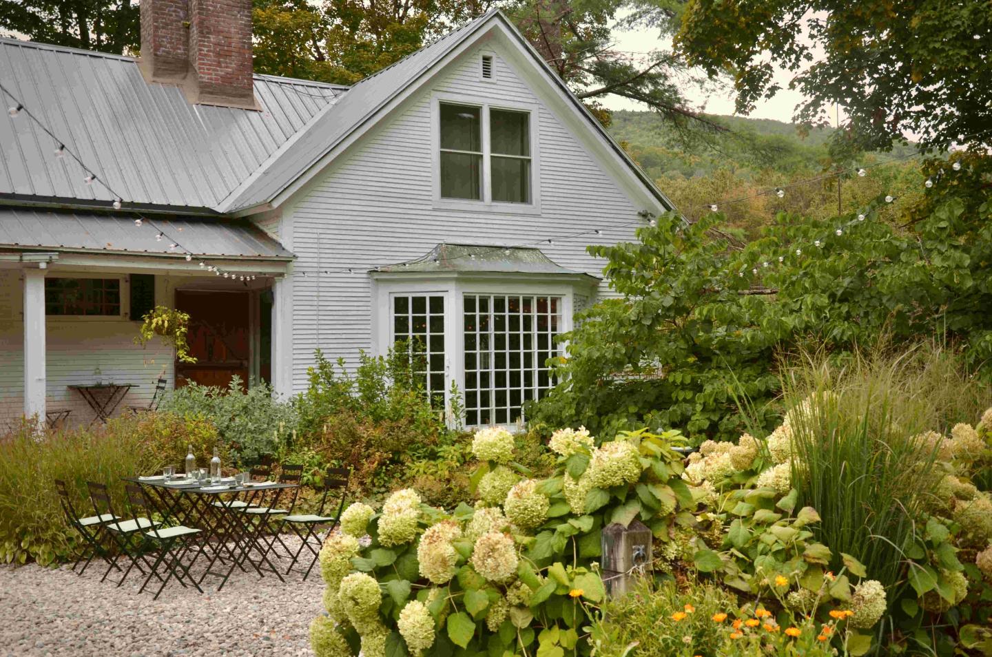 A quaint white house with a lush garden and blooming hydrangeas.