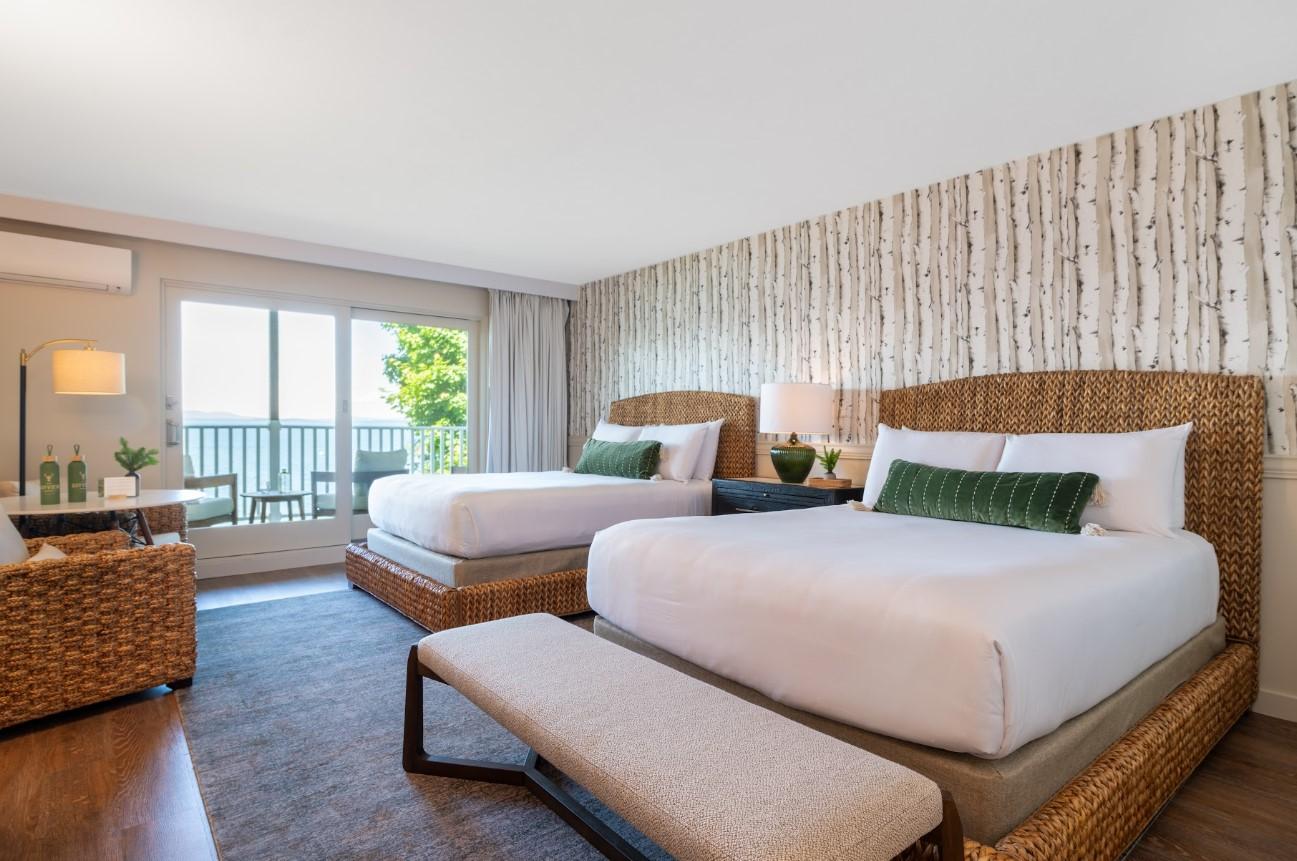 Two double beds in a cozy hotel room with a view of the balcony and greenery.