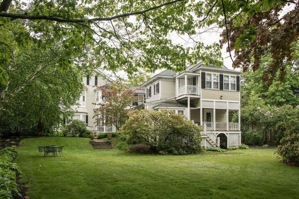 Two-story white house with a lush green lawn and surrounding trees.
