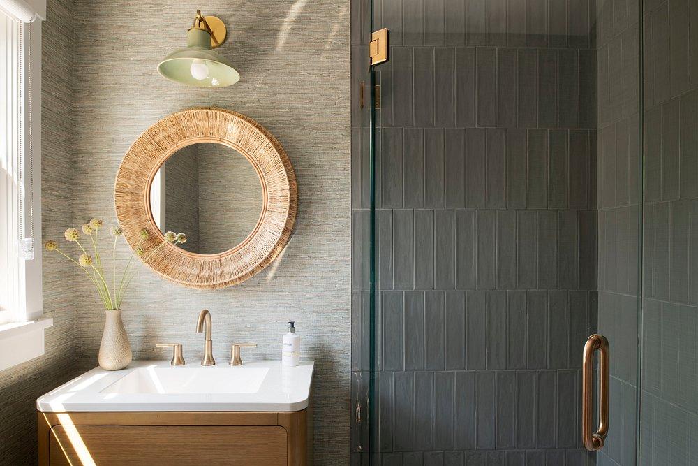 Cozy bathroom with round mirror, sink, and glass shower door.