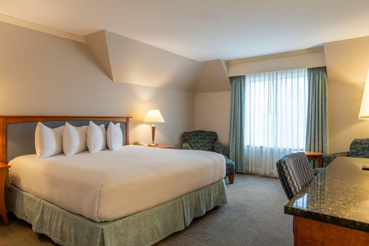 King-sized bed in a hotel room with chairs, desk, and soft lighting.