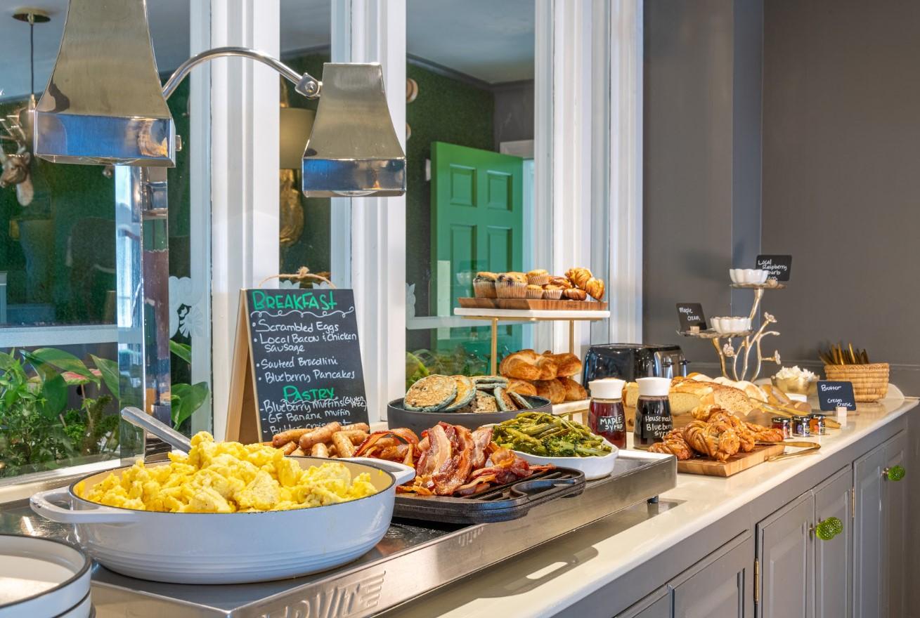 Buffet breakfast with eggs, bacon, pastries, and fruit, set on a countertop.
