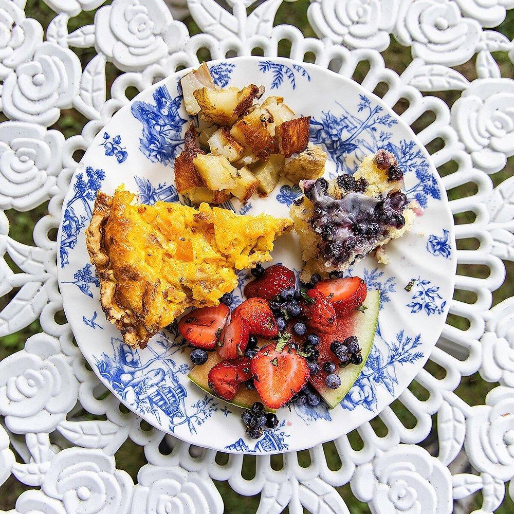 Plate with quiche, potatoes, fruit, on a floral table.