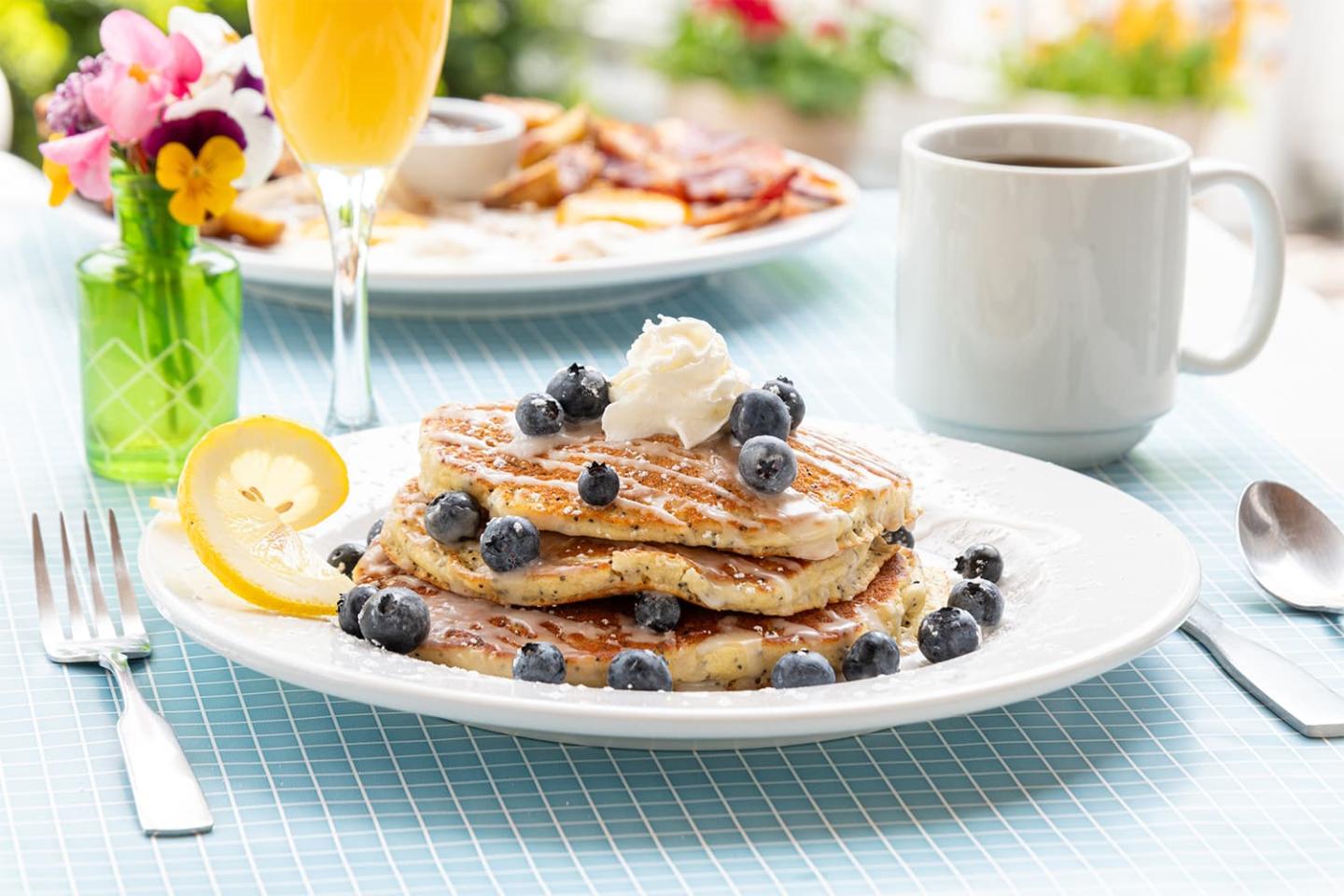 Blueberry pancakes with cream, orange juice, and coffee on a table.