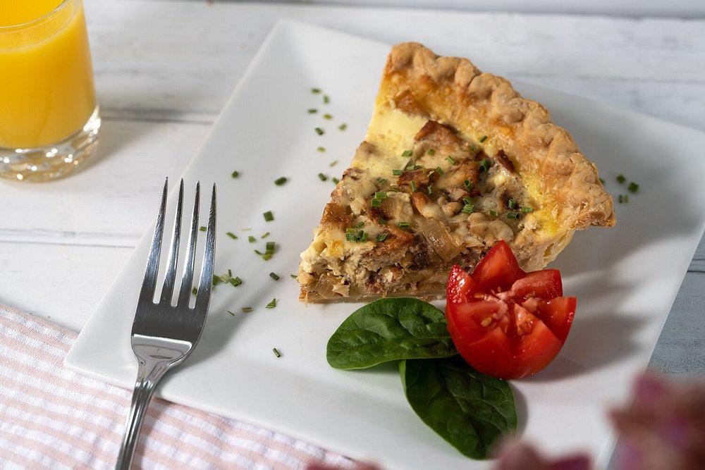 Quiche slice garnished with tomatoes and spinach, fork, and glass of orange juice.